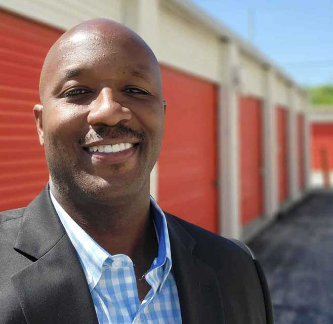 public storage district manager smiles while standing outside drive up storage units